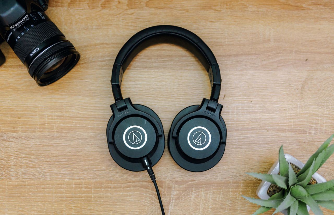 about-img Top view of black headphones, camera, and potted plant on a wooden table, representing modern technology essentials.