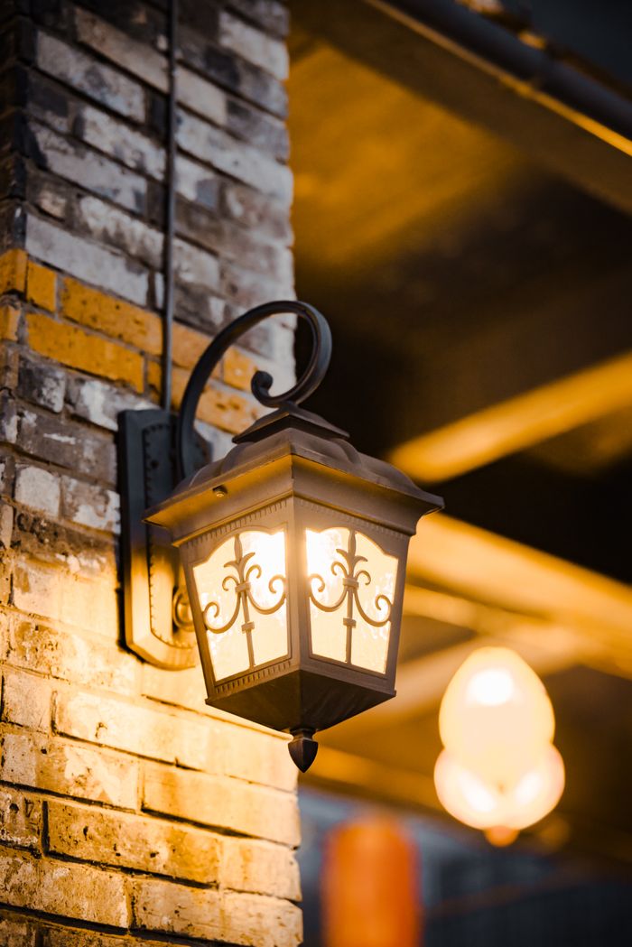 Vintage lantern illuminating a rustic brick wall, creating a warm ambiance in a cozy outdoor setting.