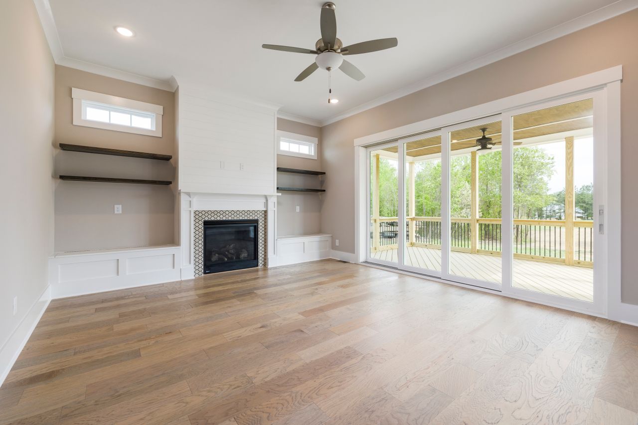 Spacious living room with fireplace and ceiling fan overlooking veranda through glass doors.